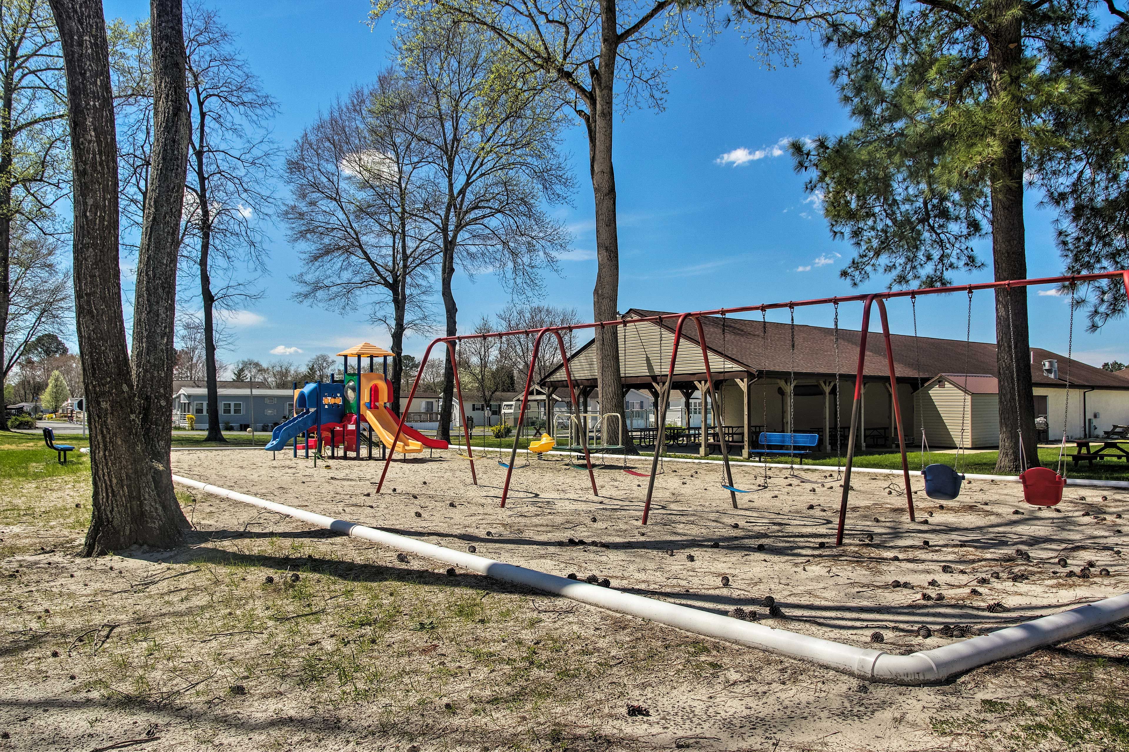 Un parque infantil con columpios y tobogán, rodeado de árboles y un edificio al fondo.