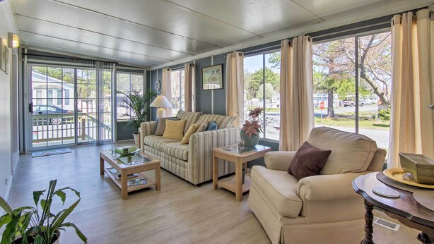 Un salón amplio con sofá, sillones y una mesa de centro. Ventanas grandes ofrecen vistas al exterior.