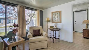 Una sala de estar con un sillón color beige, una mesa de centro de cristal, una mesita de noche con lámpara e impresión botánica enmarcada en la pared.