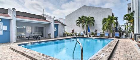 A swimming pool with a brick border, palm trees, and a building with a white facade.
