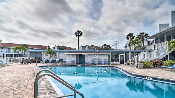 A swimming pool with a brick deck, lounge chairs, and a building with a blue facade in the background.