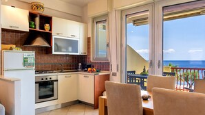 Eine kompakte Küche mit Herd, Backofen und Mikrowelle. Es gibt einen Essbereich mit Stühlen und einem Tisch sowie einen Balkon mit Meerblick.