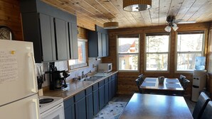 Moderni keittiö, jossa on tummat kaapit, puinen työtaso, jääkaappi sekä ruokailutila, jossa on pöytä ja tuolit.