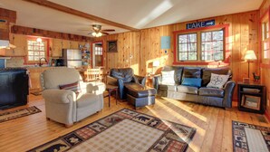 Interior acogedor de una cabaña con paredes de madera, un comedor, una sala de estar con chimenea y un letrero que indica vista al lago.