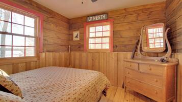 Una habitación tipo cabaña de madera con cama, cómoda y dos ventanas.