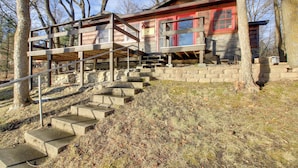 Una cabaña de exterior de madera, con base de piedra y una escalera que lleva a una terraza.