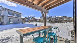 A covered outdoor seating area with a wooden table and turquoise chairs, overlooking a snowy landscape with houses and mountains in the background. - Hike, Ski, Golf, & Fish: Silverthorne Townhome! (Silverthorne)