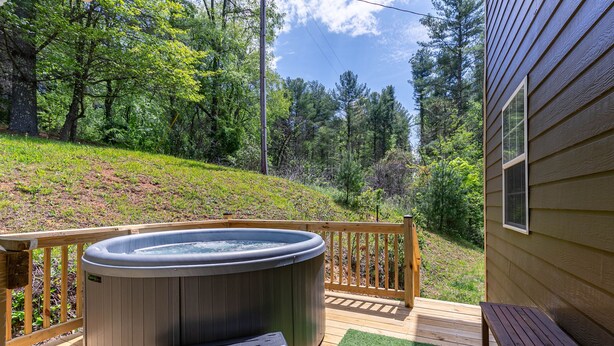 Ein Whirlpool auf einer Holzterrasse mit Blick auf einen bewaldeten Hang.