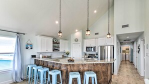 A modern kitchen with a central island, bar stools, hanging pendant lights, and a view of the adjacent living area. - Surfside Beach Home w/ Views, Steps to Shore! (Freeport)