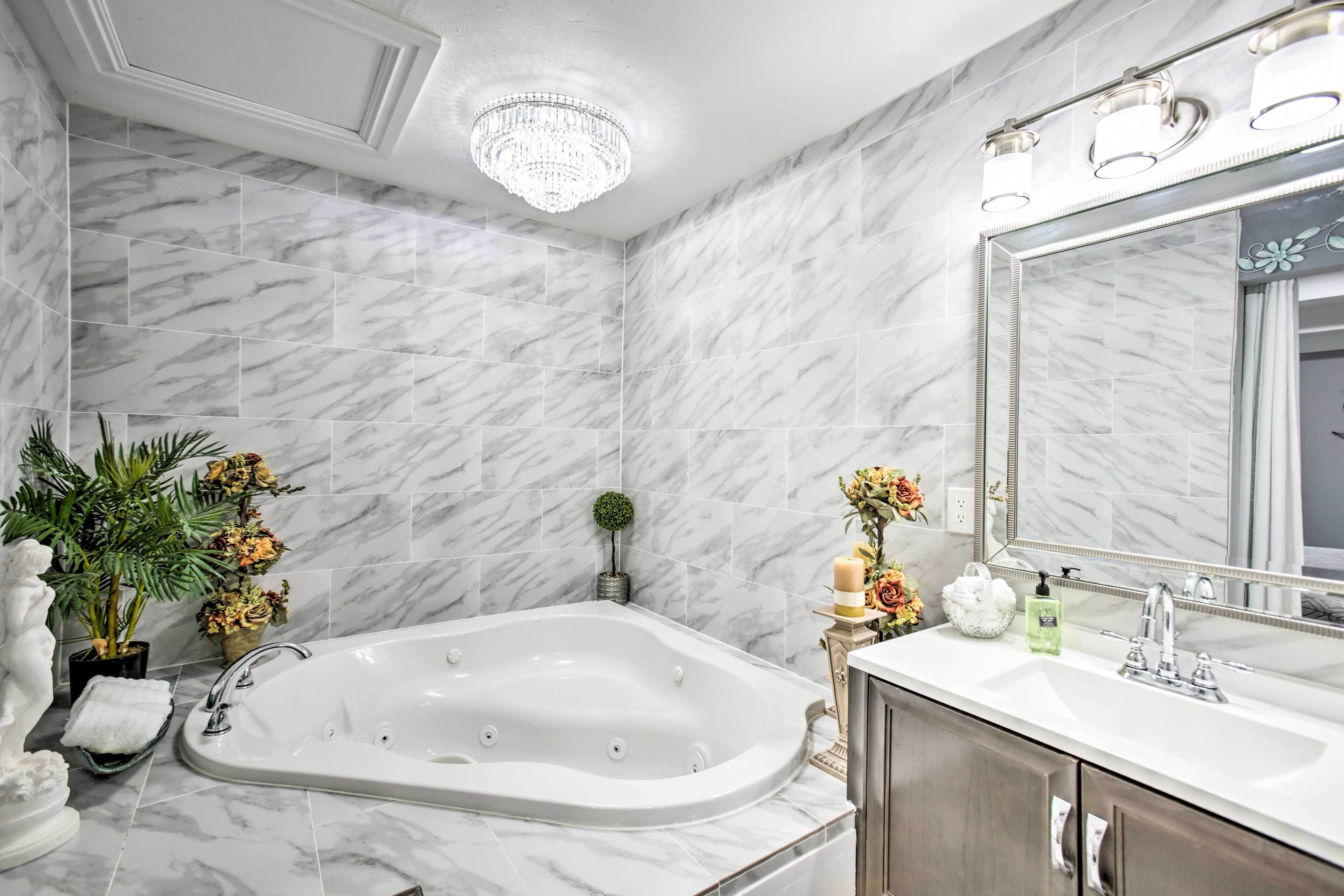 A bathroom with a marble wall, a freestanding bathtub, a large mirror, and a chandelier.