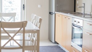 A modern kitchen with wooden cabinets, a stainless steel refrigerator, an oven, and a dining table with chairs.