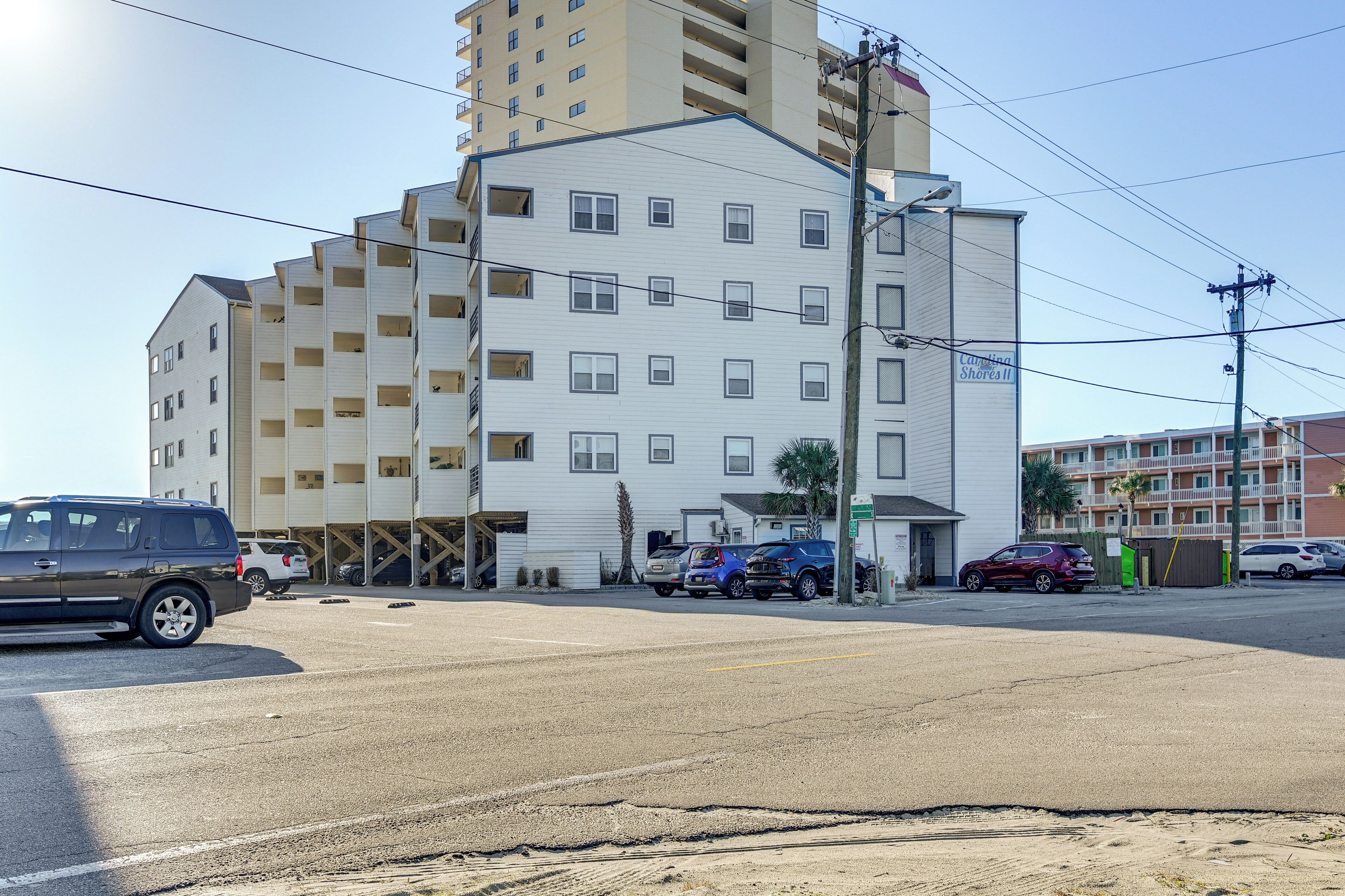 A multi-story hotel with a flat facade, several balconies, and a parking area with cars.
