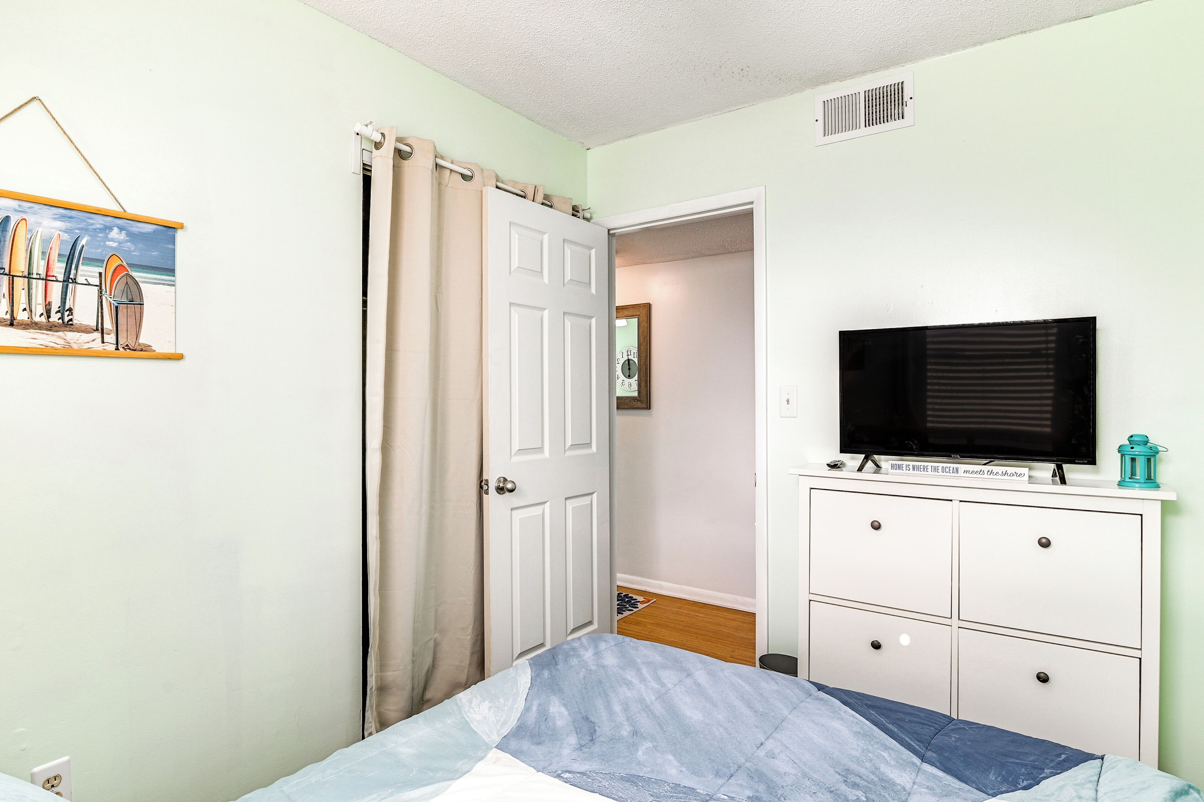 A bedroom with a bed, a television on a dresser, a door, and a painting on the wall.