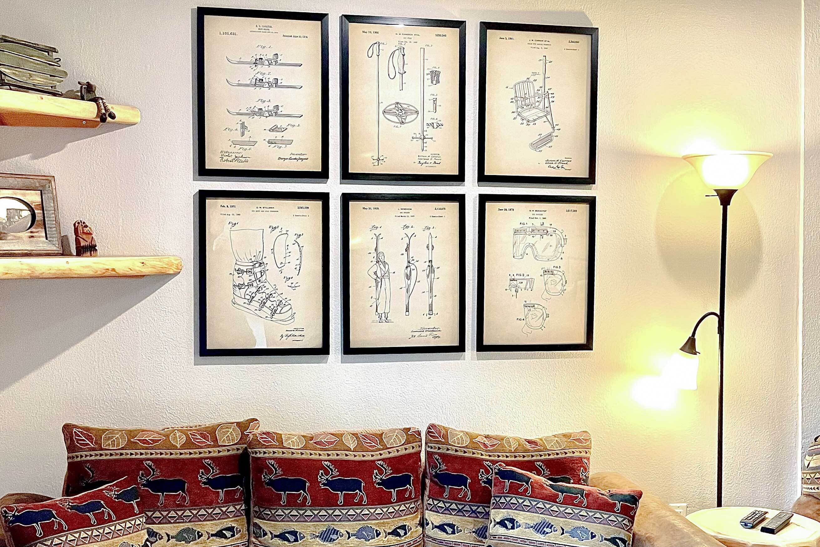 A room with six framed technical drawings on the wall, a lamp, and a couch with patterned cushions.