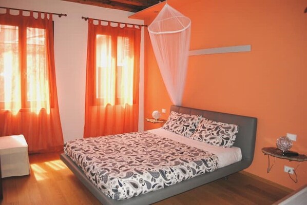 Une chambre à coucher avec un lit, des rideaux orange, une table de chevet et une commode.