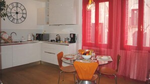 A kitchen with white cabinets, a clock, and a dining area with a table set for two. - Ca'Rosa, 500 years old, Super Central (Venezia)