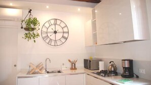 A kitchen with white cabinets, a hanging plant, a wall clock, a sink, and various appliances. - Ca'Rosa, 500 years old, Super Central (Venezia)