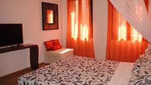 A bedroom with a bed, a TV, a window with orange curtains, and a painting on the wall. - Ca'Rosa, 500 years old, Super Central (Venezia)