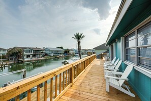 Une terrasse en bois, agrémentée de chaises Adirondack blanches, offre une vue sur une marina où sont amarrés des bateaux et où se trouvent des maisons.