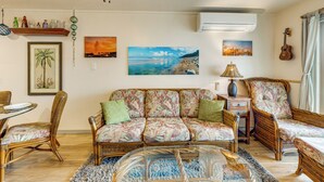 Ein Wohnzimmer mit einer Couch, Sesseln, einem Glastisch und Wandbildern.