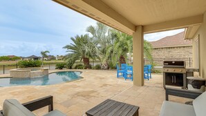 A covered outdoor area with a pool, patio furniture, and a barbecue grill.