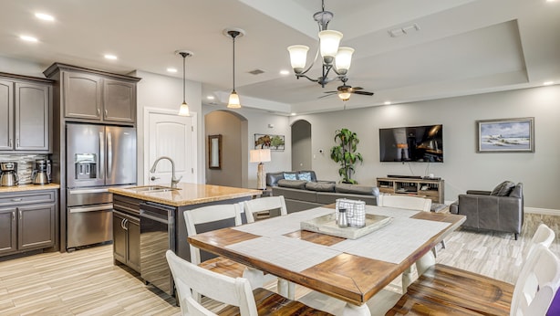 A modern kitchen with stainless steel appliances, a wooden dining table, and a living area with a TV and seating.