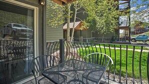 Une terrasse couverte, dotée de chaises et d’une table en métal, qui donne sur une rue où sont garées des voitures et sur un immeuble avec un balcon.