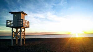 A wooden lifeguard tower on a beach with the sun setting in the background.