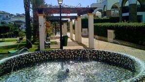 A fountain with mosaic tiles, a palm tree, and a building with arches in the background.