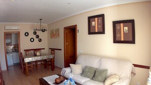 A living room with a sofa, a coffee table, a dining table with chairs, and a kitchen area in the background.