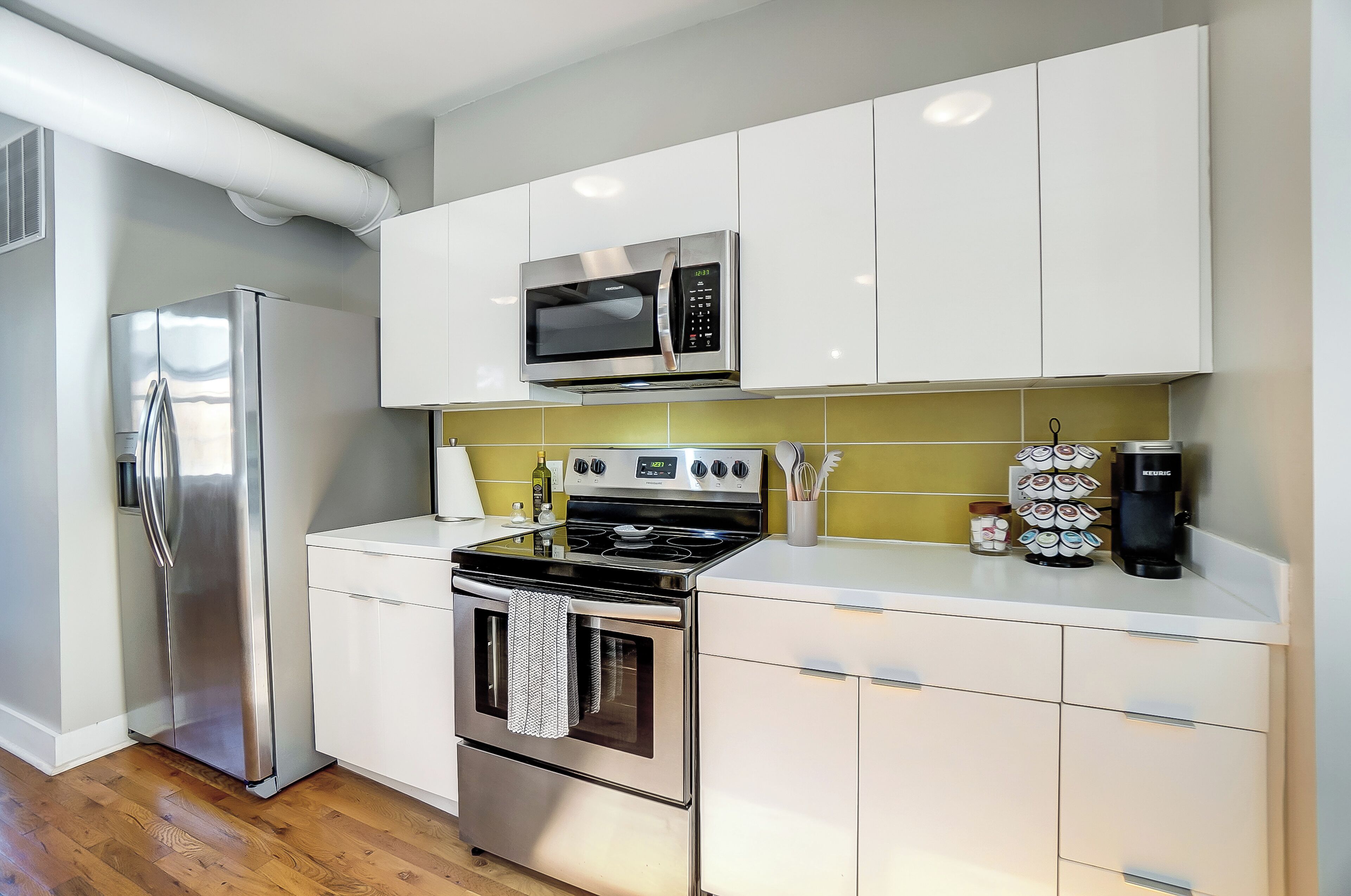 A modern kitchen with stainless steel appliances, white cabinets, and a yellow backsplash.