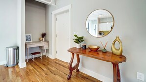 A hallway with a wooden floor, a desk with a plant, a mirror, and a small table with decorative items. - 'the Republic Retreat' Walk to Washington Park! (Cincinnati)