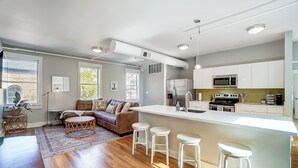 A modern kitchen with white cabinets, a stainless steel refrigerator, and a microwave. There is a wooden dining table and a sofa with cushions. - 'the Republic Retreat' Walk to Washington Park! (Cincinnati)