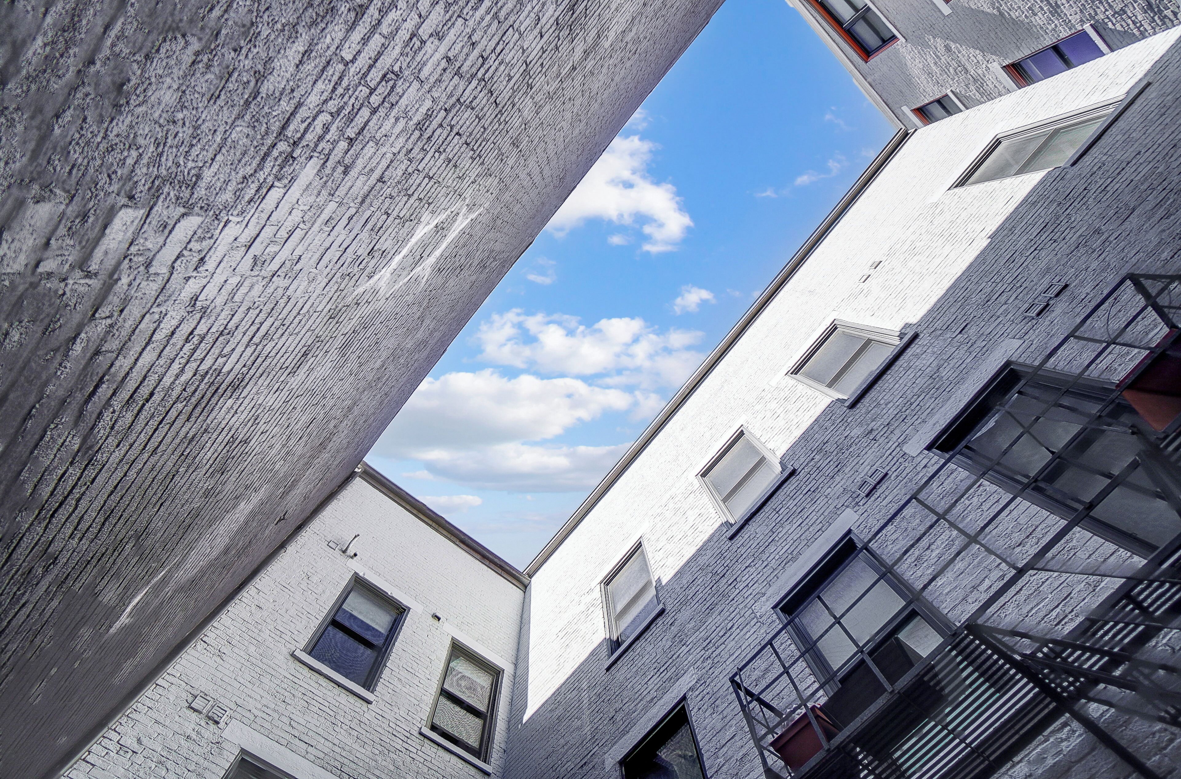 A view of a building with white brick walls and multiple windows, including a fire escape on the right side.