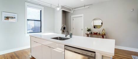 A modern kitchen with a white countertop, stainless steel dishwasher, and a window providing natural light.
