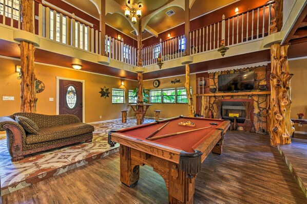 A pool table in a room with a wooden floor, a sofa, and a fireplace. - Spacious Conroe Home w/ Foosball & Pool Table! (Conroe)