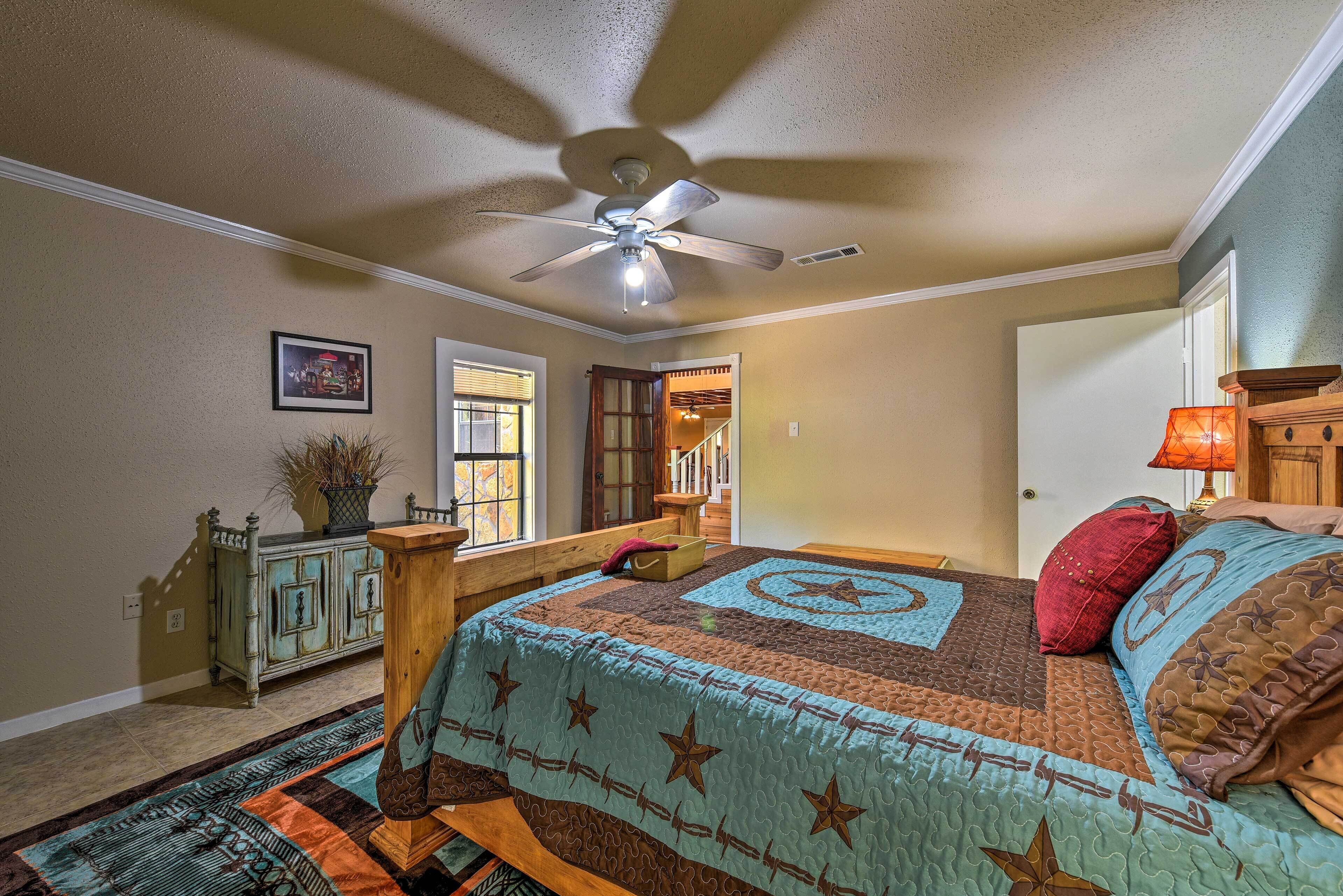A bedroom with a bed, a ceiling fan, a window, a door, and a nightstand with a lamp.