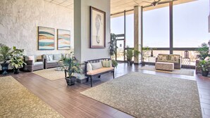 A spacious lobby with a high ceiling, large windows, and a variety of seating areas including a sofa, a bench, and a small table. - Indoor Pool & Views: Beachfront Ocean City Condo (Ocean City)