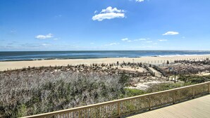 A beach view from a wooden deck with a clear sky and sandy beach in the background. - Indoor Pool & Views: Beachfront Ocean City Condo (Ocean City)