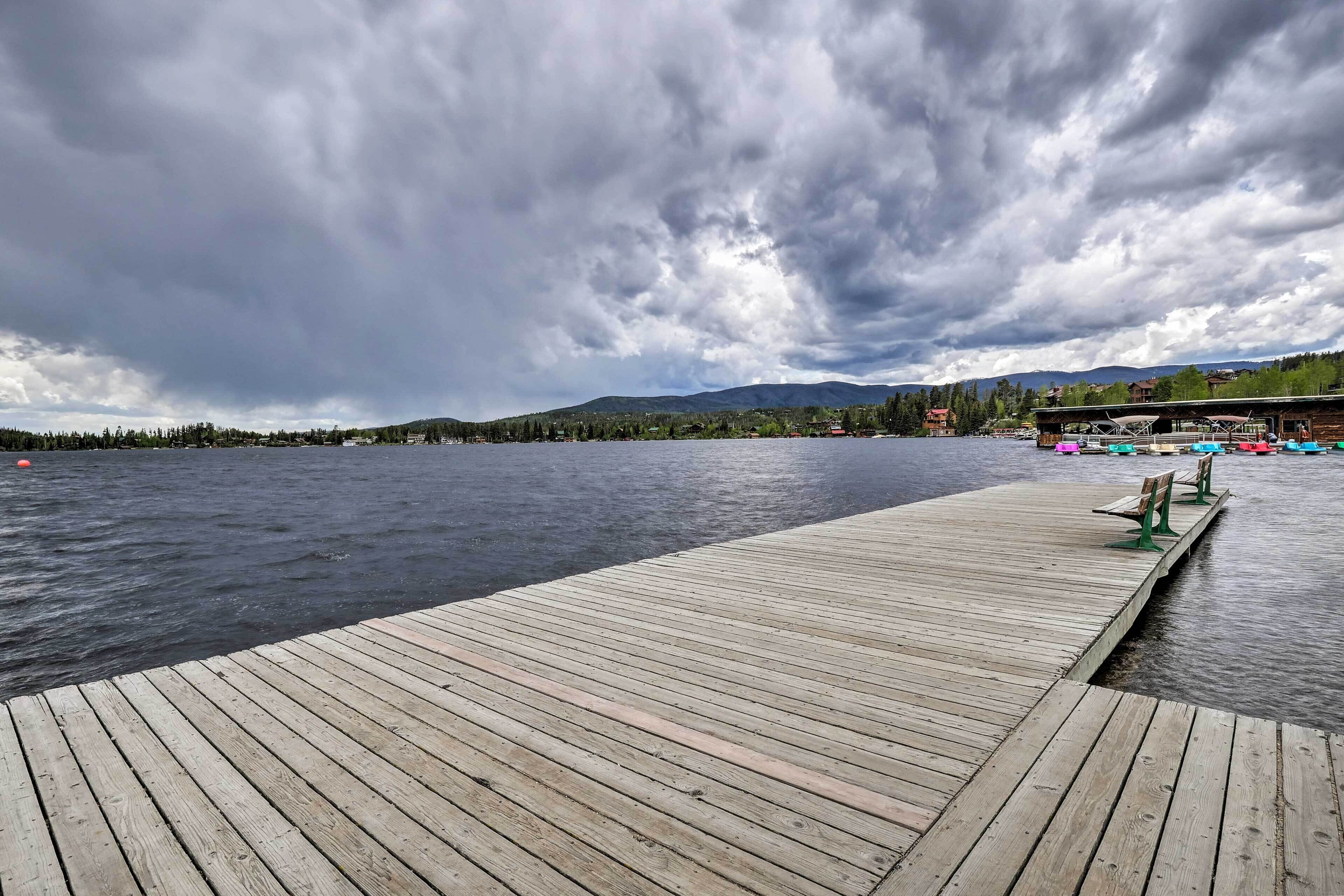 A wooden dock extending into a lake with a backdrop of mountains and a cloudy sky.