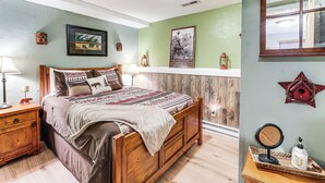 A bedroom with a wooden bed, a nightstand, a lamp, a framed picture, and a wall-mounted shelf with a decorative item. - 3 Mi to Rocky Mountain National Park (Grand Lake)