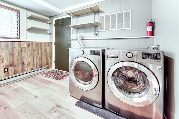 A laundry area with two front-loading washing machines, a fire extinguisher on the wall, and a vent above the machines.