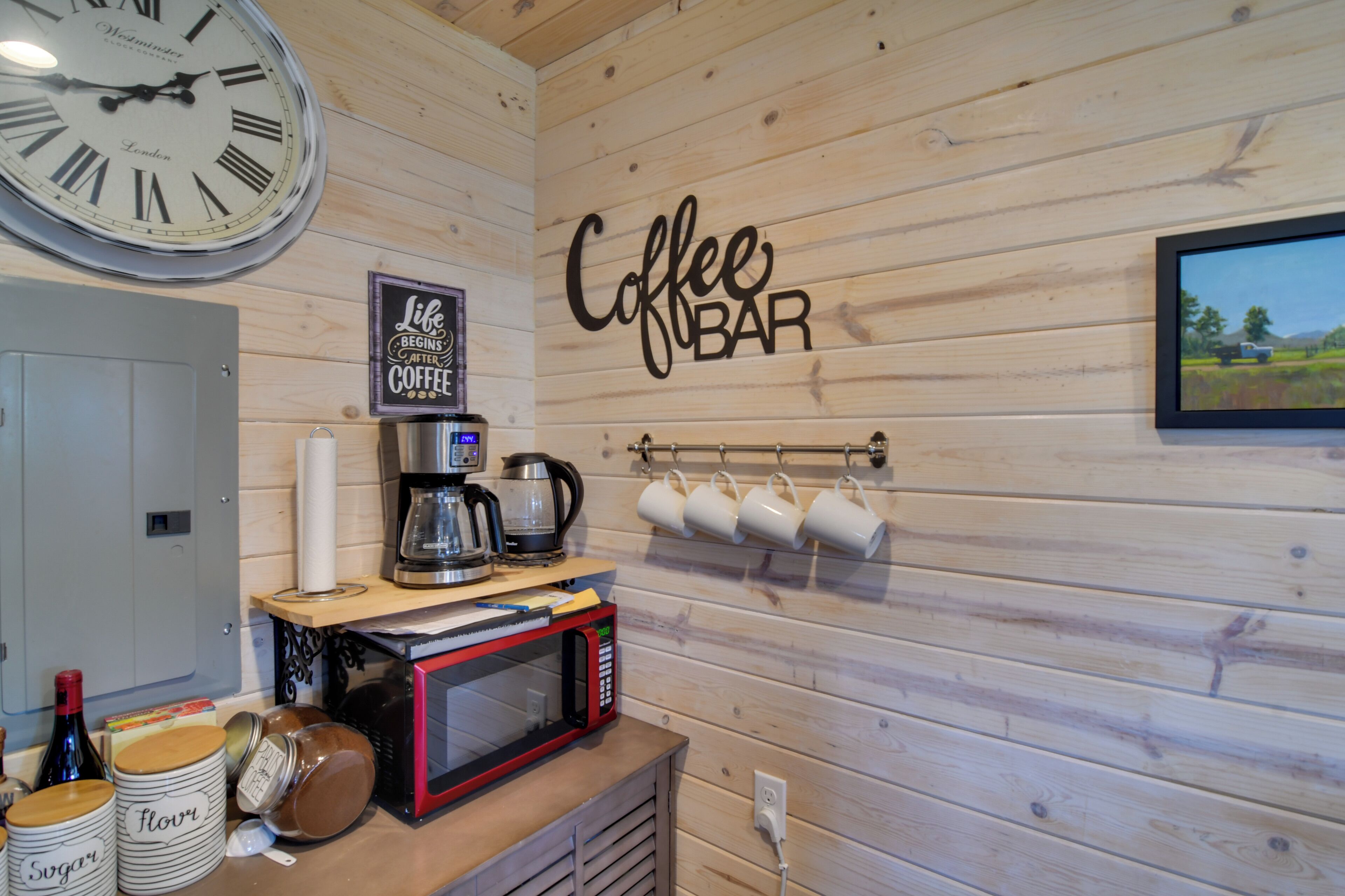 Eine Küche mit einer Uhr, einem Schild für die Kaffeebar, einer Kaffeemaschine, Tassen und Gläsern mit den Aufschriften 'Zucker' und 'Mehl'.