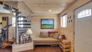 A cozy cabin interior with a wooden staircase, a sofa, a lamp, and a shelf with books and a stuffed toy. - Secluded Jefferson Cabin w/ Deck + Mountain Views! (Jefferson)