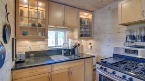 A kitchen with wooden cabinets, a stainless steel stove, and a sink. - Secluded Jefferson Cabin w/ Deck + Mountain Views! (Jefferson)