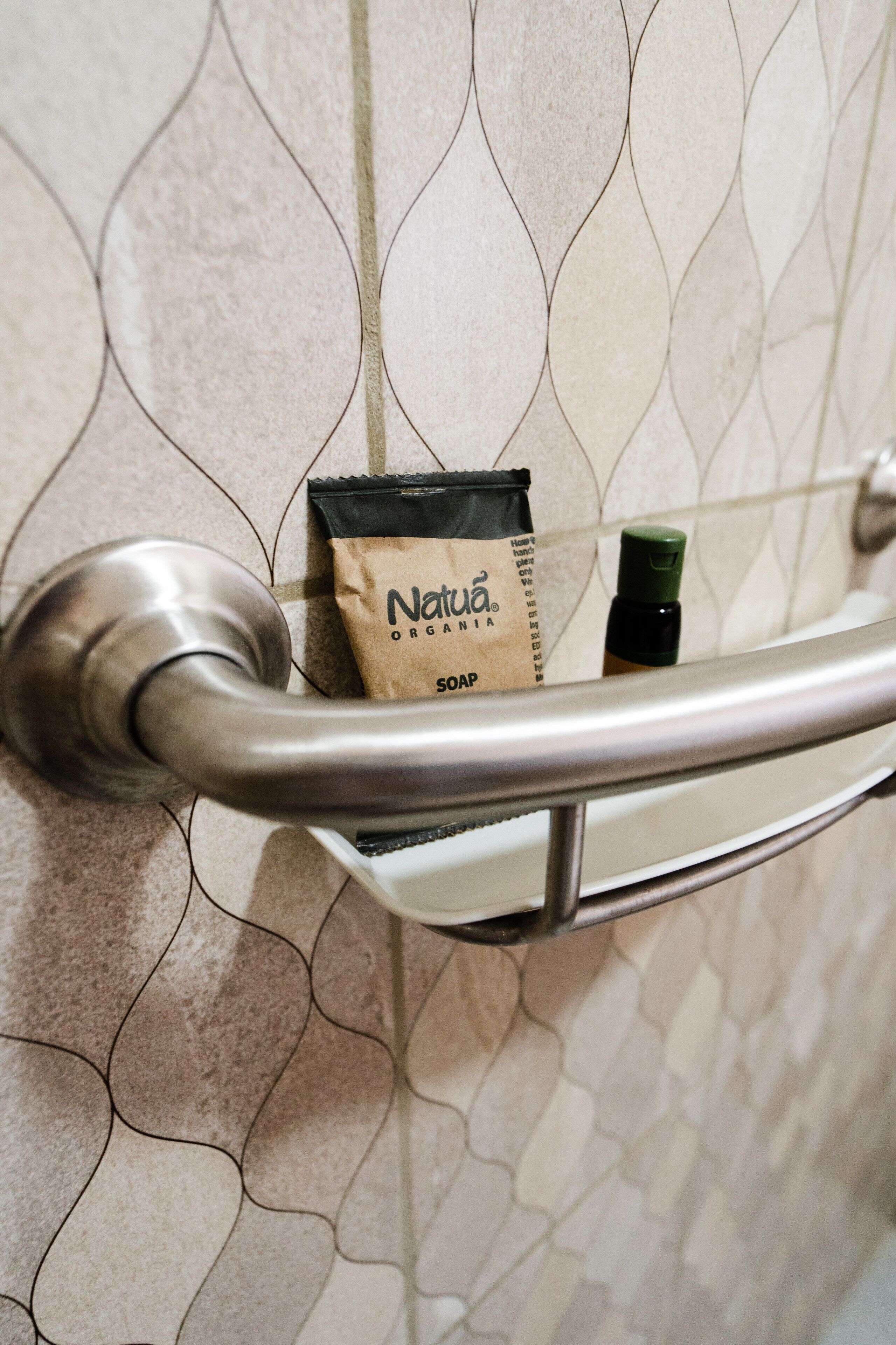 A bathroom with a shower door, a soap dispenser, and a soap bar on a shelf.