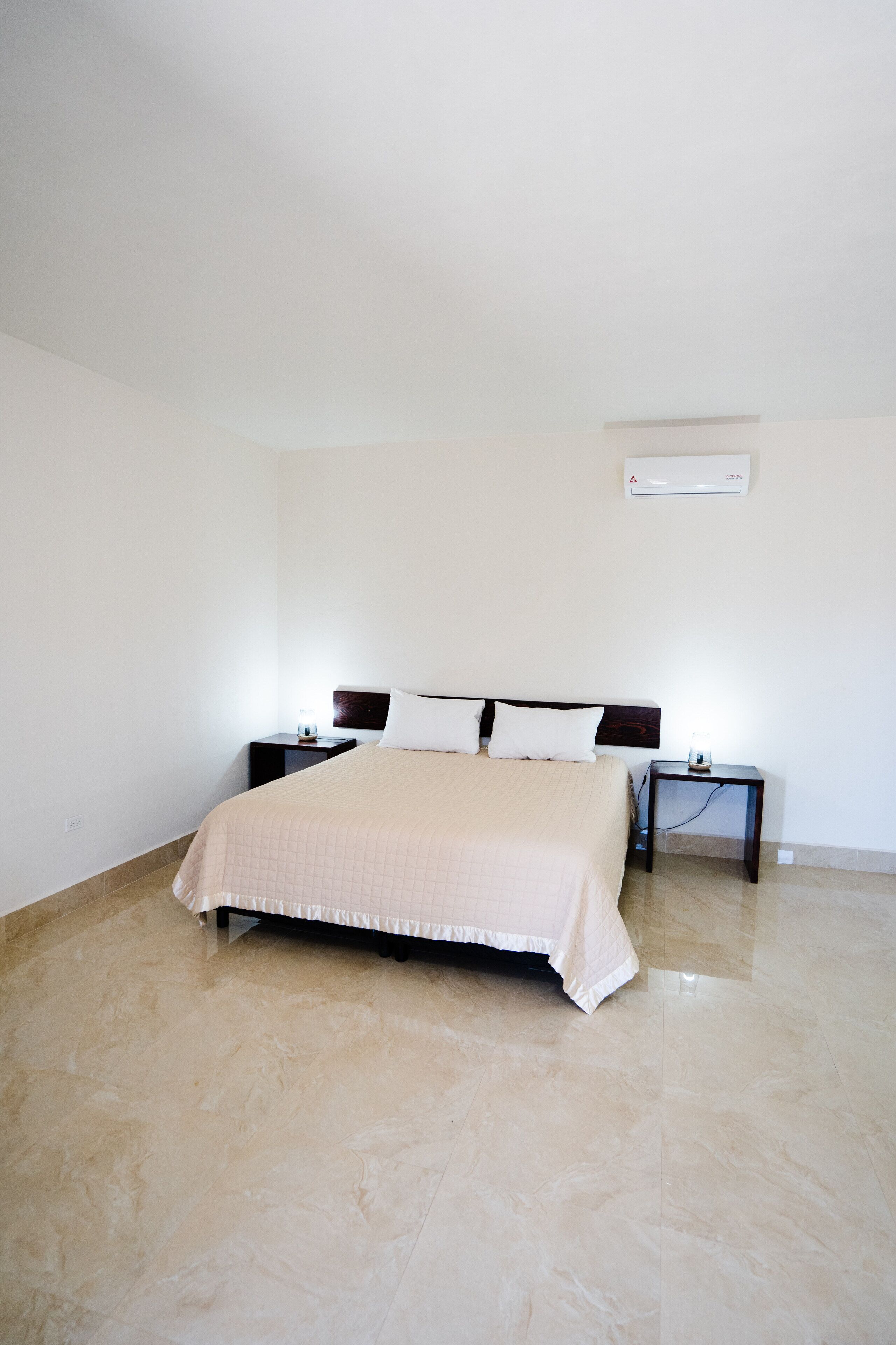 A bedroom with a bed, two bedside tables, a nightstand, and a wall-mounted air conditioner.
