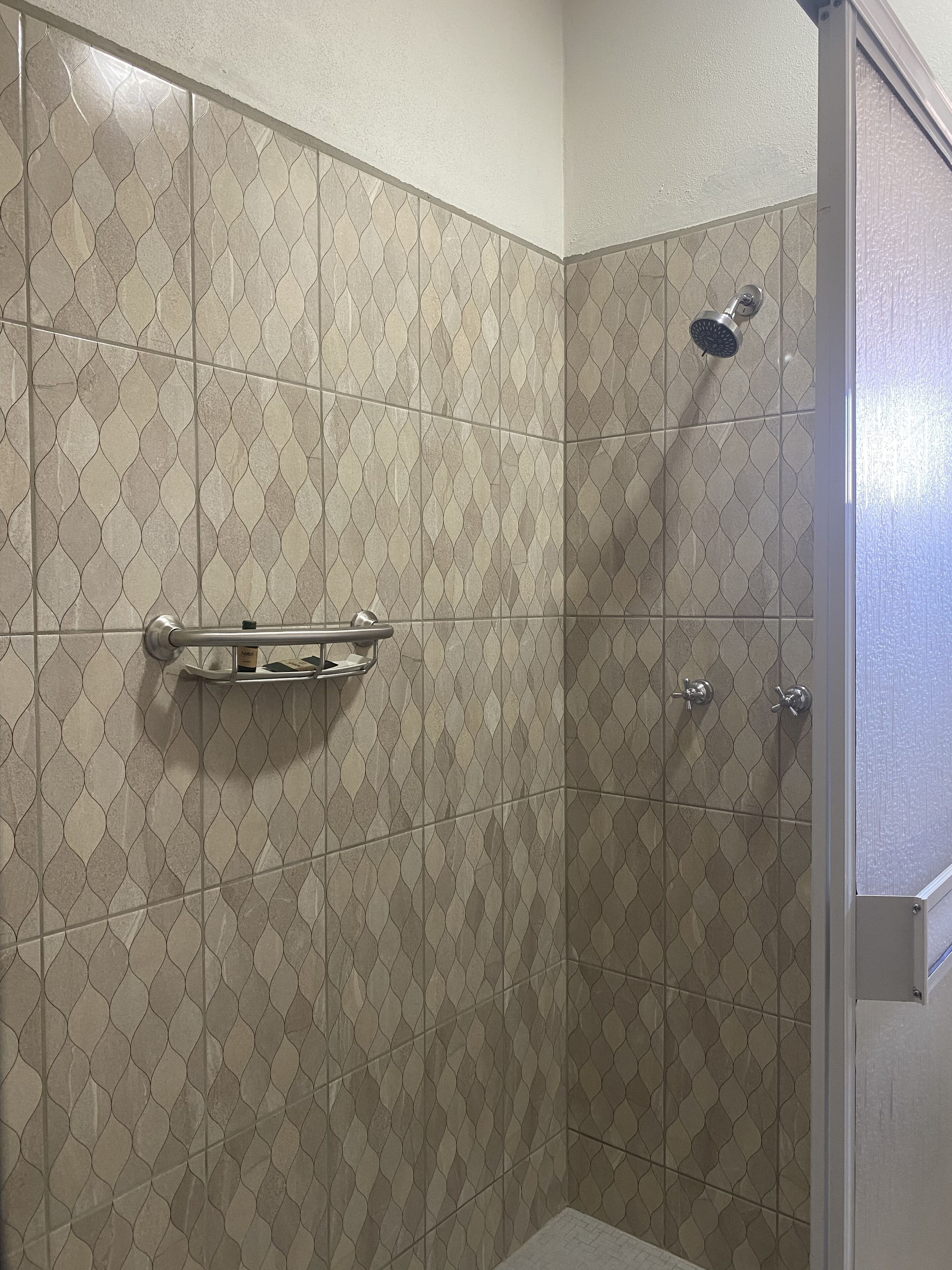 A shower with a patterned tile wall, a handrail, and a showerhead.
