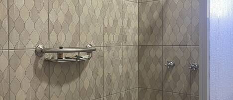 A shower with a patterned tile wall, a handrail, and a showerhead.