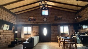 A cozy room with a bed, a sofa, a dining table with chairs, a kitchen area, and a large window. - Hotel & RV PARK Rosa Evelyn (San Quintin)